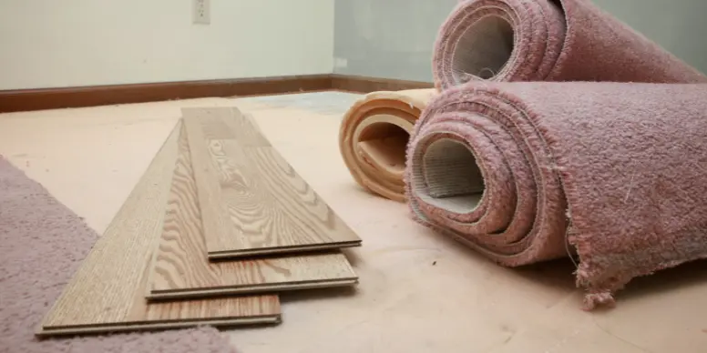 Rolled-up old carpet next to new wood flooring planks