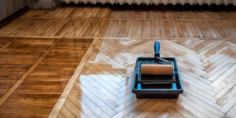 Paint roller applying a fresh coat of finish to a herringbone hardwood floor
