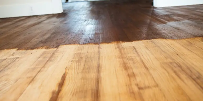 Hardwood floor half sanded, showing the dark worn finish next to fresh bare wood